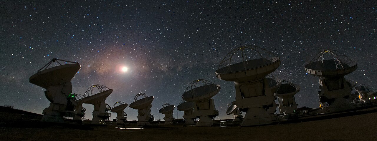 Several large radio antennas under a starry night sky.