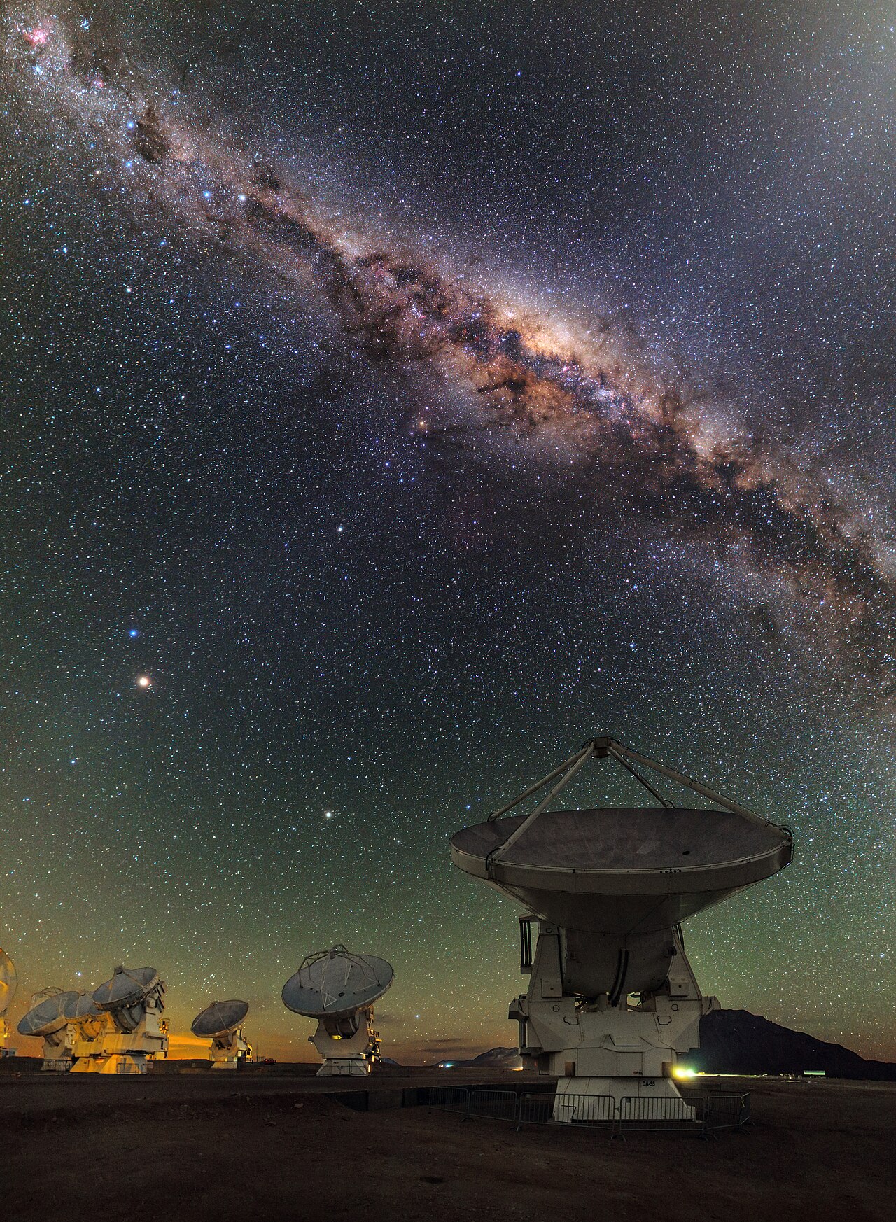 Several large radio antennas under a starry night sky with the Milky Way visible.