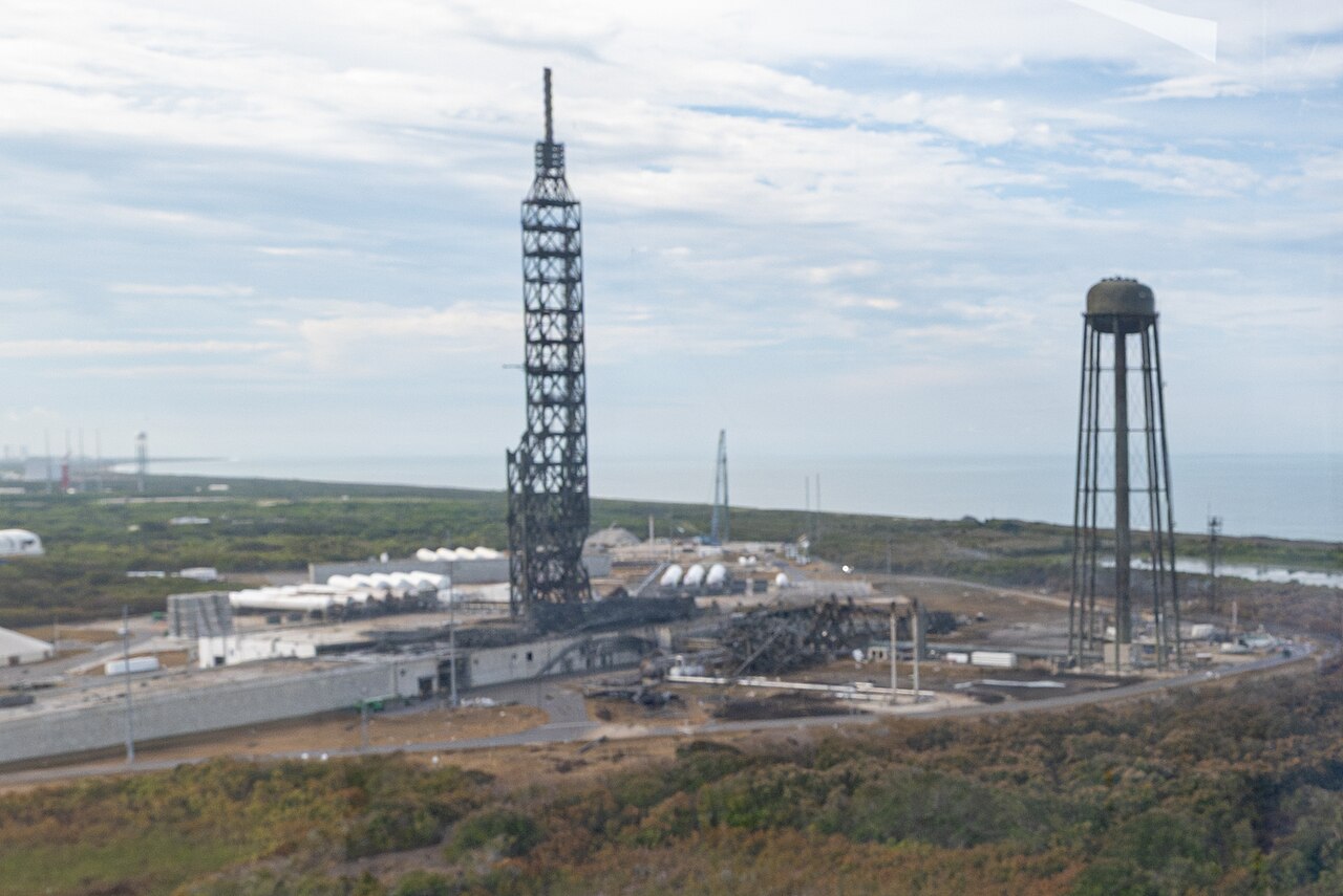 Aerial view of a damaged launch complex with bent structures and debris.